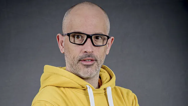 Homme à lunettes noires et sweat jaune posant devant un fond gris, illustrant un article sur les ETF PEA.